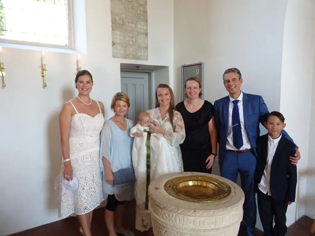Barnedåb i kirke med familie samlet omkring døbefonten og baby i dåbskjole til en smuk og personlig dåbsdag.