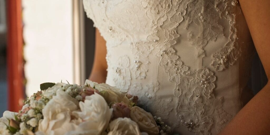 Brudekjole med blonde- og perledetaljer samt brudebuket med hvide blomster
