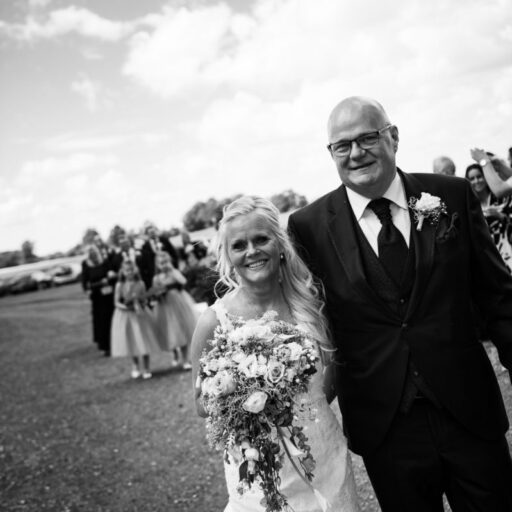 Smilende brudepar går sammen med brudebuket i hånden