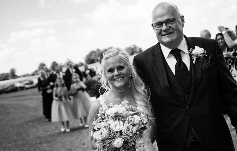 Smilende brudepar går sammen med brudebuket i hånden