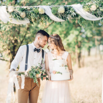 Brudepar med bryllupskage og blomster i hånden ved udendørsbryllup