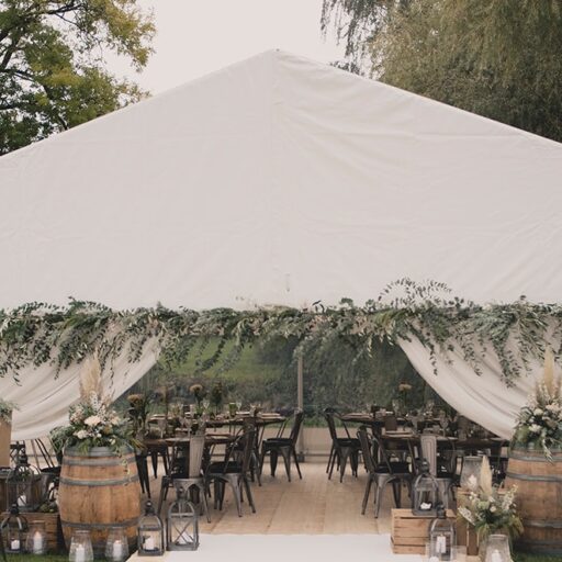 Hvidt telt klar til bryllup med rustikke borde og grønne grene langs indgangen